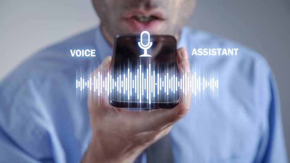 A man in a blue shirt speaks into a smartphone, with visual indicators for voice command and an assistant graphic displayed.