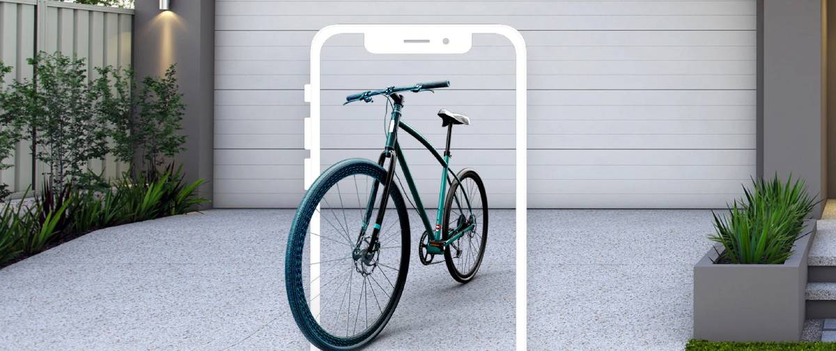 A smartphone displays a sleek bicycle in an outdoor setting with a textured concrete surface and lush greenery nearby.