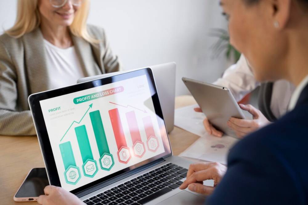 A group of professionals collaborates over a laptop displaying a colorful profit and loss chart with graphs and icons.