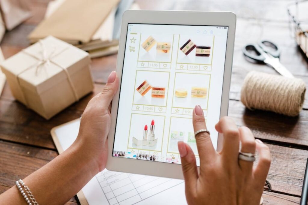 A person browsing beauty products on a tablet, with packaged gifts and crafting materials on a wooden table.