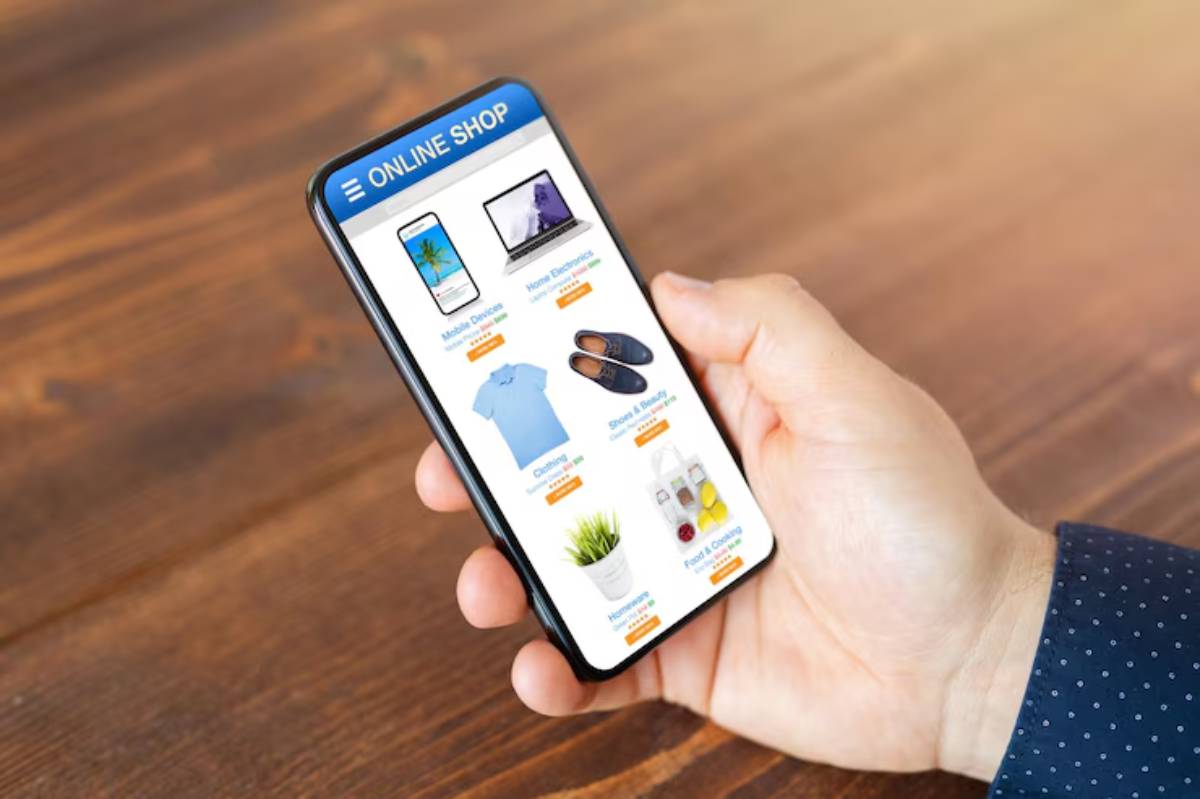 A hand holds a smartphone displaying an online shop with various product categories, including clothing and electronics.