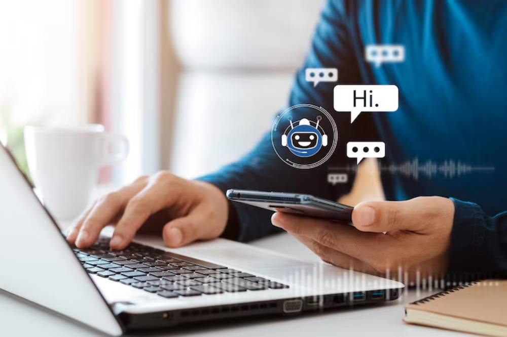 A person using a smartphone while typing on a laptop, with speech bubbles indicating a conversation with a chatbot.