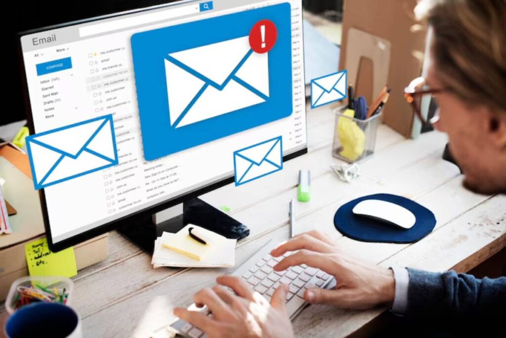A person types on a keyboard in front of a computer displaying an email interface with multiple unread message notifications.