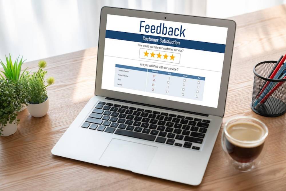 Laptop displaying a customer satisfaction feedback form with ratings, surrounded by a plant and coffee cup on a wooden desk.