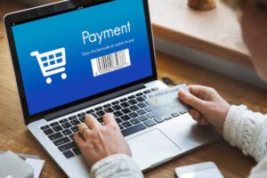 A person holding a credit card above a laptop displaying a payment screen with a shopping cart and barcode for checkout.