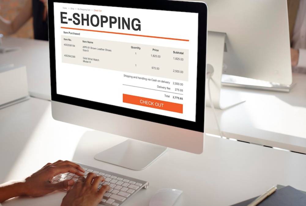 A person's hands on a keyboard, viewing an online shopping cart with items, prices, and a total bill on a computer screen.