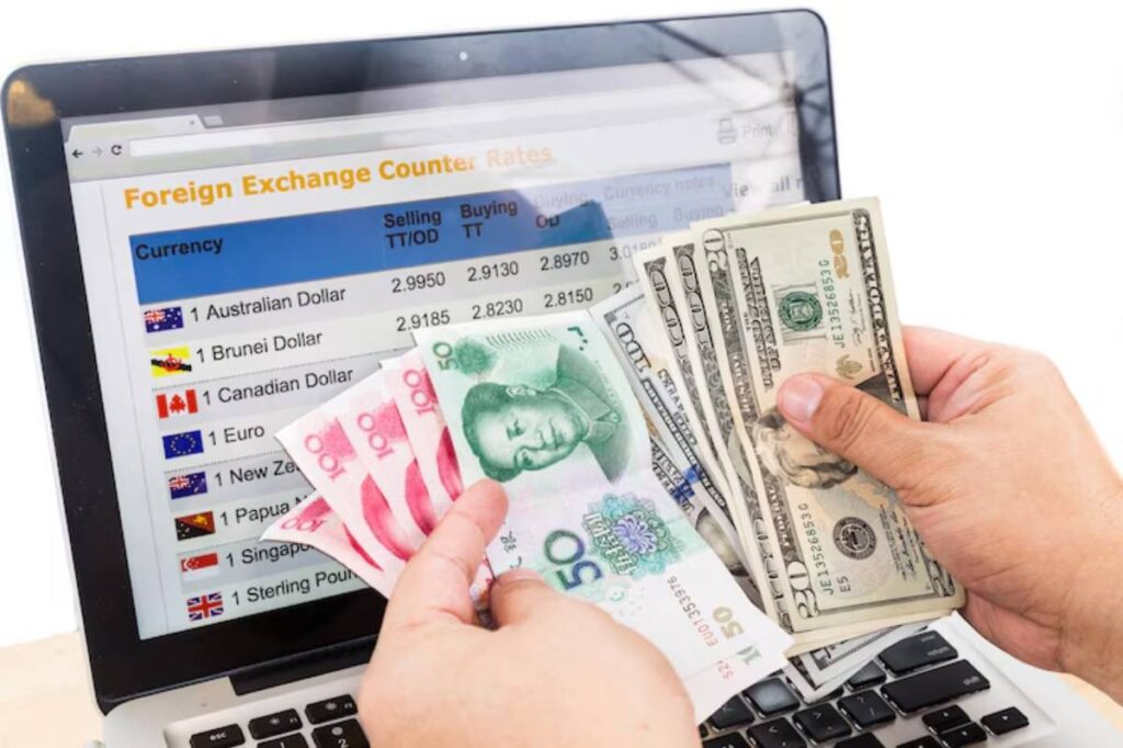 A person holding various banknotes in front of a laptop displaying foreign exchange rates for multiple currencies.