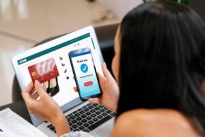 A person using a laptop for online shopping, holding a credit card, while displaying a successful payment confirmation on their smartphone.