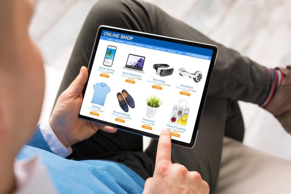 A person listing products on online shop on a tablet, displaying categories like electronics, clothing, and home goods.