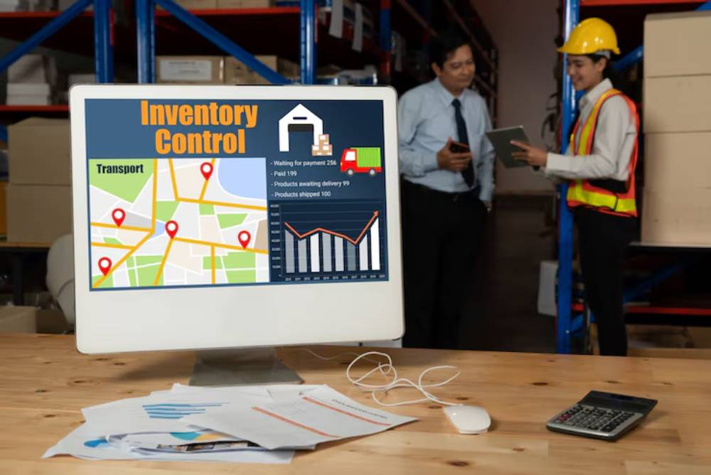 A computer monitor displays an inventory control dashboard with graphs, a map, and transport details in a warehouse setting.