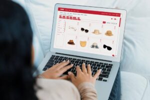 A person search for products online for women's accessories, browsing a variety of hats and sunglasses on a laptop.