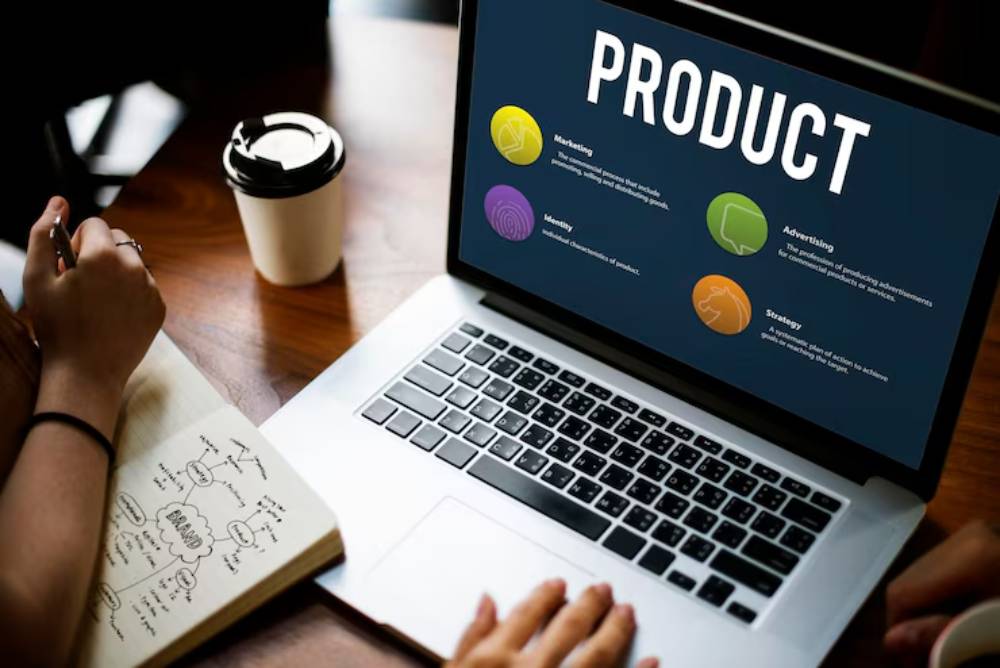 A laptop displaying a 'PRODUCT' presentation with sections on Marketing, Identity, Advertising, and Strategy, beside a notebook and coffee cup.