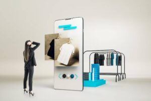 A woman in business attire looks at clothing options displayed on a smartphone, with a clothing rack in the background.